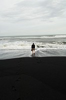 Iceland, Vik village, church, man with feet in the sea at the black sand beach.