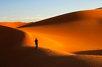 Tourist walking at sunset in the sand dunes of the Erg Muzuruq, Sahara desert, Libya