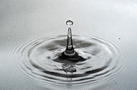 A drop of water falling into a pool forming a classic column with drops  Close up