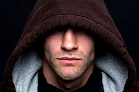 An evil looking man wearing a hooded top with his eyes hidden against a black background