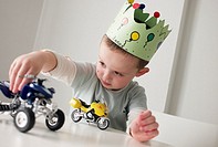 Boy with a crown in his birthday playing with cars on a table.