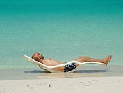 Young man, bald with a beard, lying in a hammock in the sun on the edge of the Caribbean beach in Cayo Levisa Cuba.