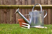 Gardening still life of a watering can hand fork and terracotta pot on the lawn