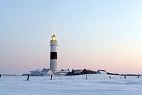 Lighthouse Kampen on snow covered fields with a bright blue sky during sun set, in operation with the light beam visible, Sylt, Northfrisian Islands, ...