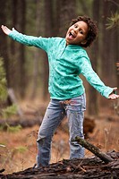 Young African American child outside in a wooded area with both arms outstretched and she is singing.