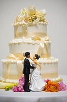 Dolls representing a bride and a groom stand in front of a wedding cake