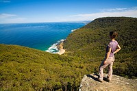 Australia, New South Wales, Royal National Park  Female hiker walking the coastal path takes a break to look down on Werrong Beach from a rocky lookou...