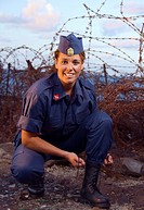 Military girl tying her boots with a spike fence in background