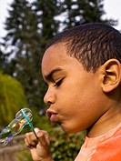 5 yr old multiracial boy blowing soap bubbles through soap wand  side view, Vertical