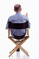 Rear view of smartly dressed mature man sitting in a directors chair  Isolated