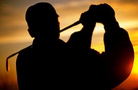 Silhouette of golfer swinging golf club at sunset