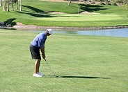 Golfer with iron club looking at putting green in distance about to hit ball over water hazard