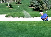 Golfer hitting ball out of sand trap, ball in air heading toward green