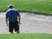 Golfer raking sand trap after hitting ball out, rear view