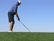 Golfer looking at target addressing ball with driver, blue sky in background