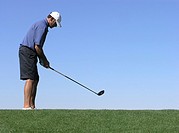 Golfer with driver setting up to hit ball off of tee, blue sky in background