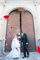 A just married couple coming out of the church with people throwing rice and rose petals to them.