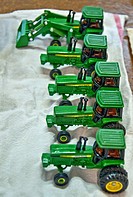 This vertical image shows a row of 5 green John Deere vintage toy tractors being prepped for an antique show, freshly washed and drying on a towel Foc...