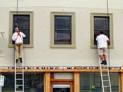 Two painters on ladders painting the window frames of an historic shop warehouse in Melville Street, Hobart, Tasmania