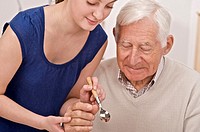 young woman, home help, or grand daughter helping a senior man or grandfather to hold a spoon to eat