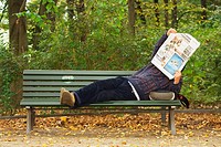 Man reading a newspaper lying on a bench in Tiergarten