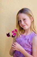 Portrait of nine-year old blonde blue eyed girl with freckles smiling while holding purple flowers