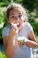 Happy young girl eating ice-cream from a cup
