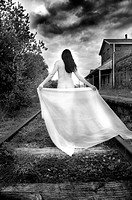 Unclothed female walks along train track with a drape trailing behind