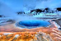 Crested Pool´s colors shine during the winter at Yellowstone National Park as Grand Geyser erupts in the background.