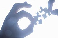 Hand holding jigsaw piece silhouetted and ijn blue tones