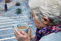 UK, Europe Senior woman holding a warm drink looking out of the window on a cold snowy day in winter