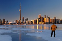 Man standing on frozen Lake Ontario ice looking at Toronto city skyline at sunset