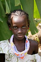Portrait of an African girl with white spots on her face looking at the lens with banana leafs as background, Tanji Village, Tanji, Gambia, Africa