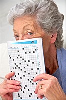 senior woman in a mauve cardigan, holding a crosswords magazine in front of her at home