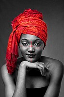 Beautiful traditional African-American woman wearing a authentic tribal red orange head scarf and red dotted makeup, supporting her chin with hand, is...