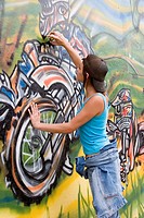 Beautiful Brazilian girl spray painting a mural on the side of a building