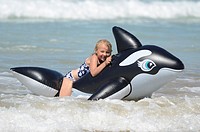 Six year old girl at the beach playing in the surf on inflatable Orca Mimiwhangata Northland, New Zealand