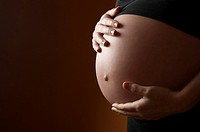 pregnant woman caressing her belly with orange background
