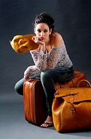 Young woman posing, sitting in a studio with two suitcases of leather and leather yellow cap, looking straight at the camera with the face of boredom,