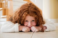 Portrait of five year old girl with red hair lying on tiles on floor
