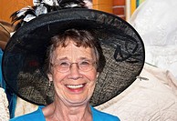This happy and active elderly woman in her seventies is smiling while trying on a big black vintage hat while shopping