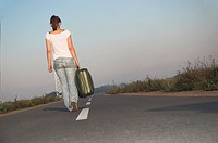 Young woman carrying suitcases on road, rear view