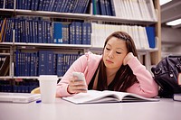 Young Asian woman using her smart phone while studying in a library.