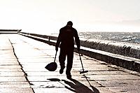 A cleaner walks along the harbour wall, slowly sweeping up rubbish left by fishermen the day before