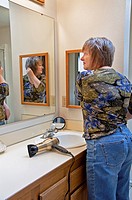 This middle aged Caucasian woman is fixing her hair after blow drying it in the bathroom, looking in a mirror  An everday grooming moment lifestyle st...