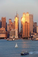 The setting sun reflects off the windows of Manhattan skyscrapers on 42nd street in New York City, New York, USA as viewed over the Hudson River from ...