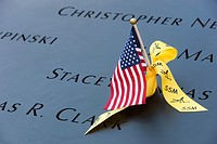 A small American flag and a yellow ribbon left on the names inscribed in the perimeter of one of the pools at the National September 11 Memorial in Ne...