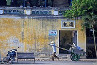 Man in conical hat pulls hand cart along street Hoi An historic town mid Vietnam