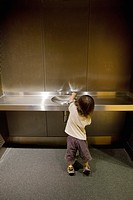 A small child trying to get a drink of water at a water fountain