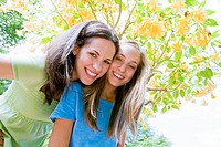 Young mother and teenaged daughter smiling happily under a flowering tree